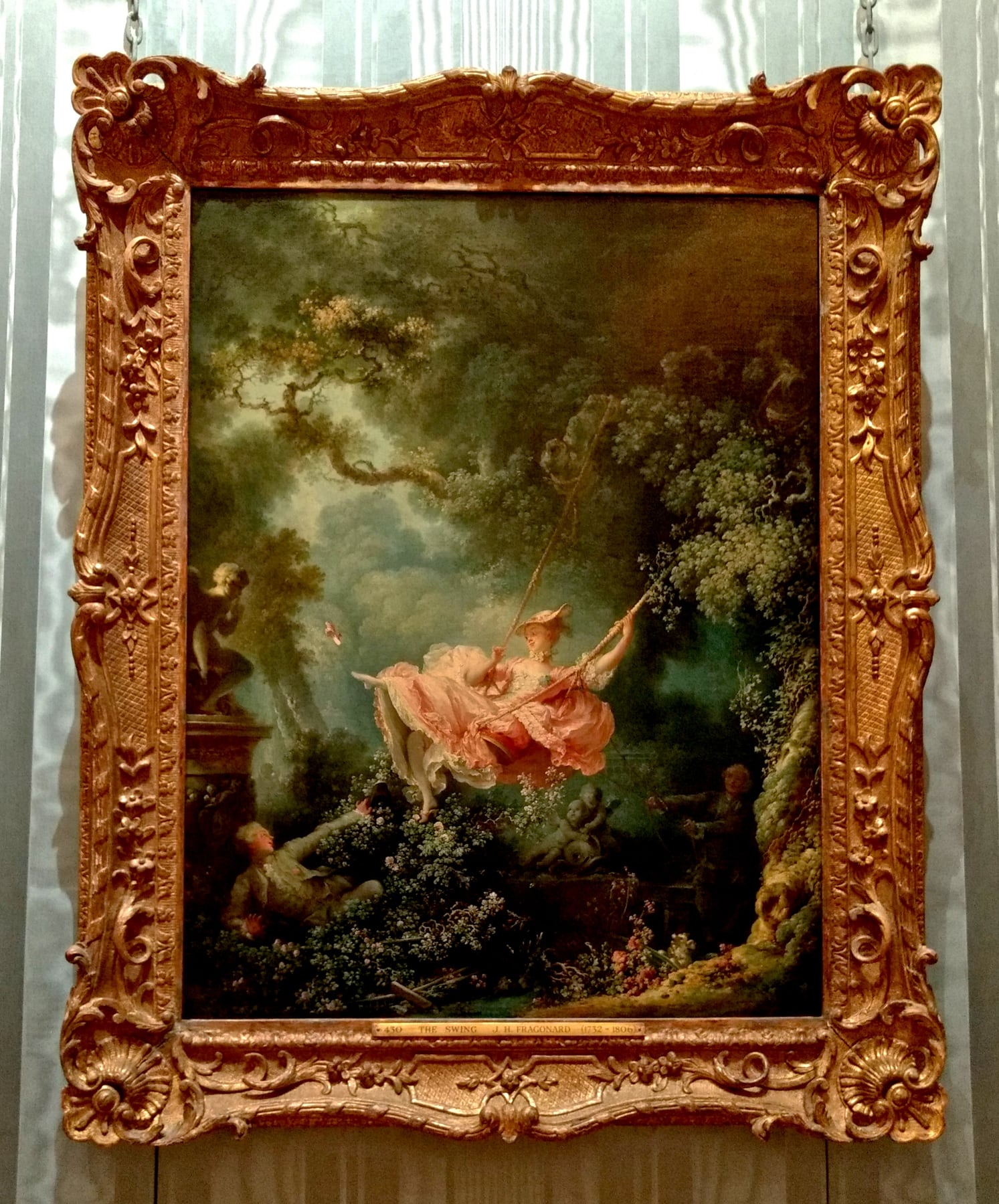 一幅装在华丽金色画框里的油画，挂在展厅的墙上：茂密的树林里，一位穿粉红色长裙的女子坐在秋千上高高荡起，一只鞋飞了出去；左下角的草丛里躺着一个男子，正抬头看她。