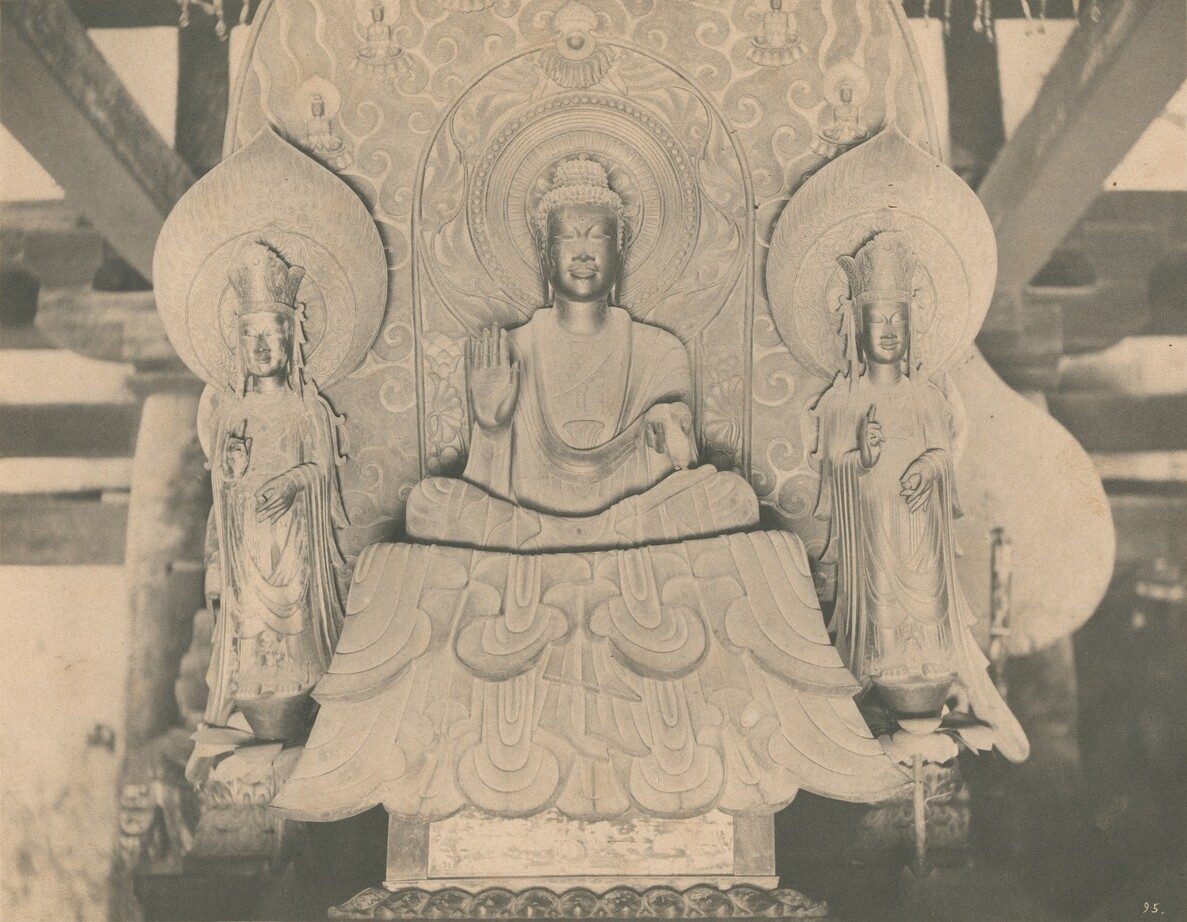 一张老照片：一尊坐佛居中，两侧各立一尊菩萨，三尊共用一个巨大的、刻满火焰纹的舟形背光；坐佛的衣裙从台座上垂下，形成对称的层层褶纹。