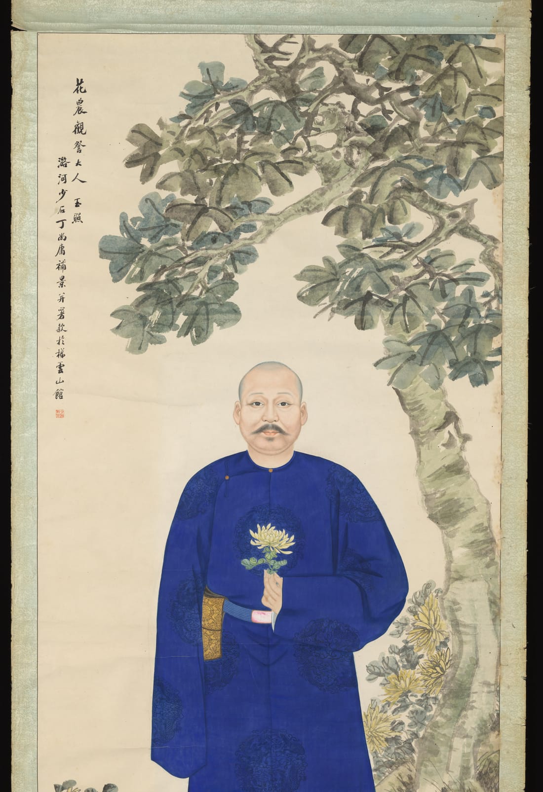 一幅立轴肖像：一位剃发留须的中年男子正面站立，身穿深蓝色长袍，左手拈着一朵黄菊；他身后一棵梧桐树弯过头顶，脚边有一丛开花的菊花。左上方有几行竖写的题字。