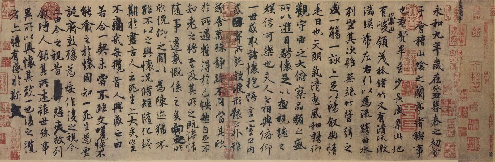 一段横长的书法手卷：浅黄褐色的纸上，墨色的行书从右往左一列列写下去，二十多列，字有大有小、有浓有淡；卷首和接缝处盖着许多红色印章。