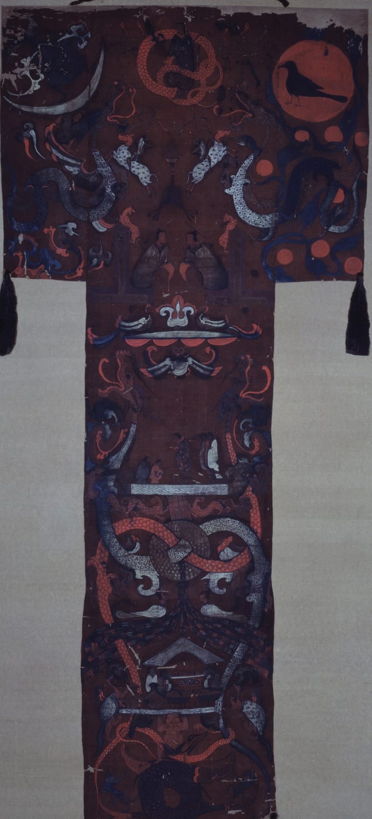 一幅深红褐色丝绢上的 T 形画：上部横宽，右上角是一轮红日，日中站着一只黑鸟；左上角是一弯白色新月；中间有一个红色盘曲的人首蛇身像。下面竖长的部分里，有一个拄杖的妇人和侍从，一块被两条龙穿过的璧，再往下是摆着器物的场景，最底下一个人托起一块平台。