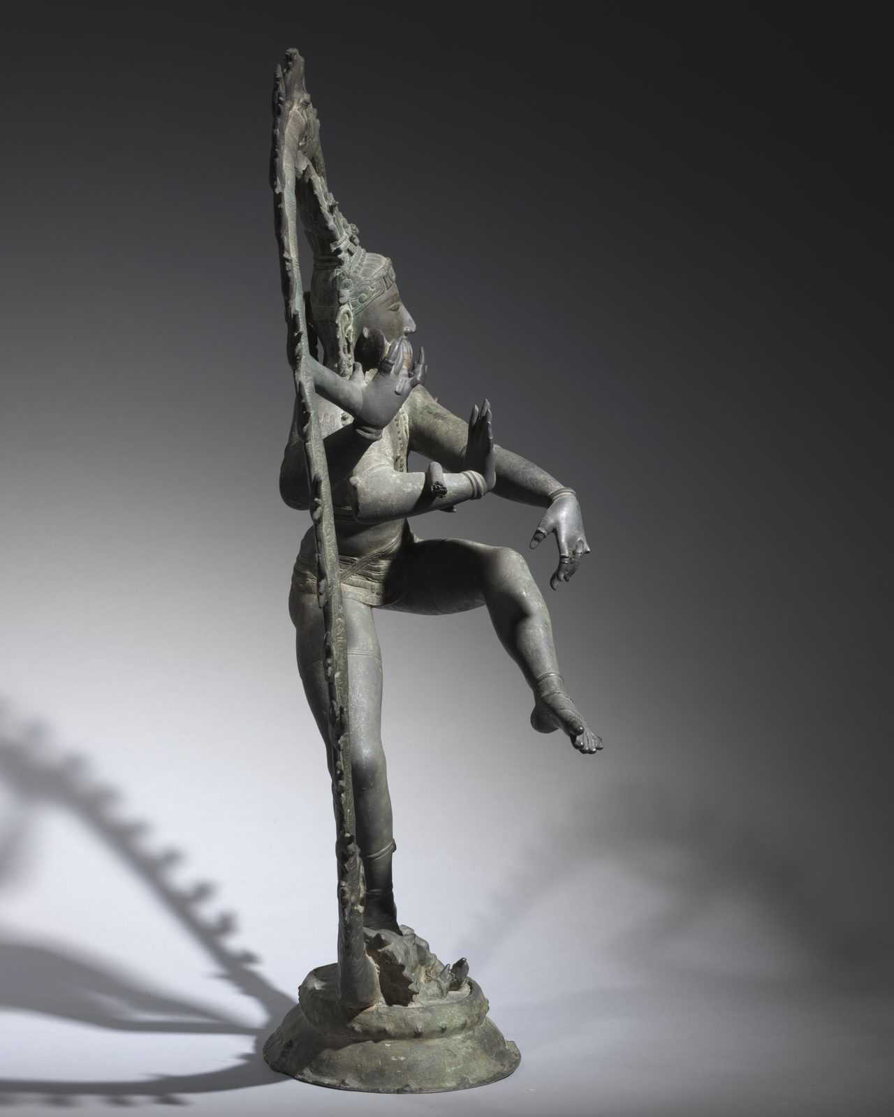 同一尊铜像的侧面：从这个角度，圆环变成一条细细的竖线，神像的身体和抬起的腿在圆环前面向外伸出，显出很深的立体感。