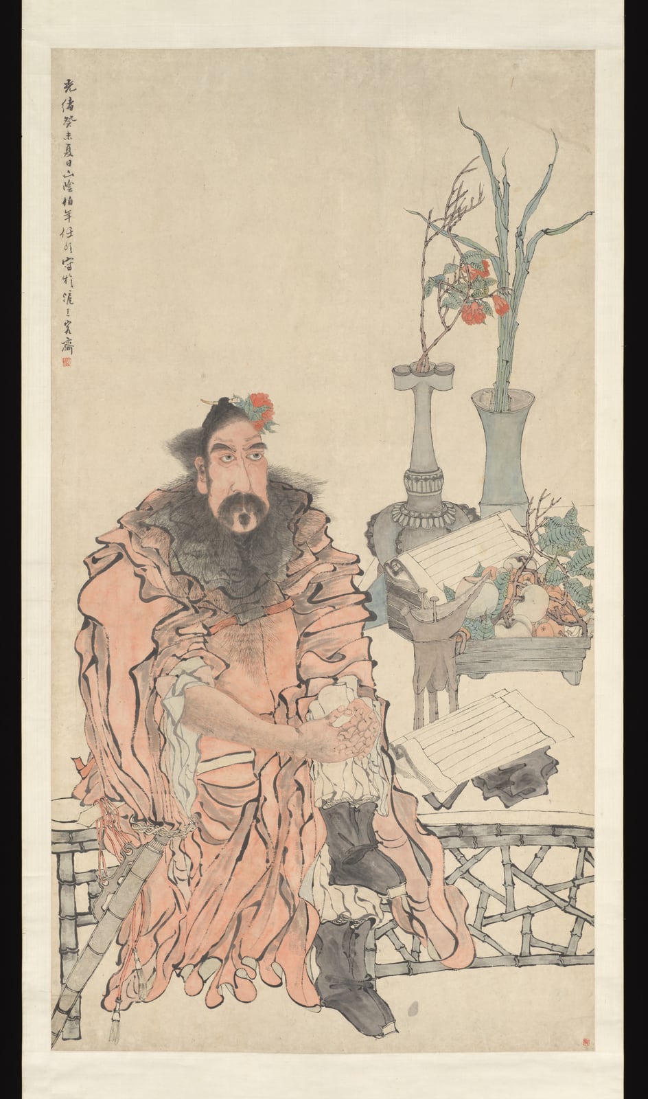 一幅竖长的立轴设色人物画：一个满脸络腮胡、浓眉大眼的大汉坐在竹木栏杆前，穿着宽大的粉红色袍子，两手交握在胸前，帽边插着一朵红花。他身旁的案上摊着一本书，摆着两件古铜器，一件插着花枝和竹叶，一件高瓶旁放着一盘果子。左上角有一行竖排题款。