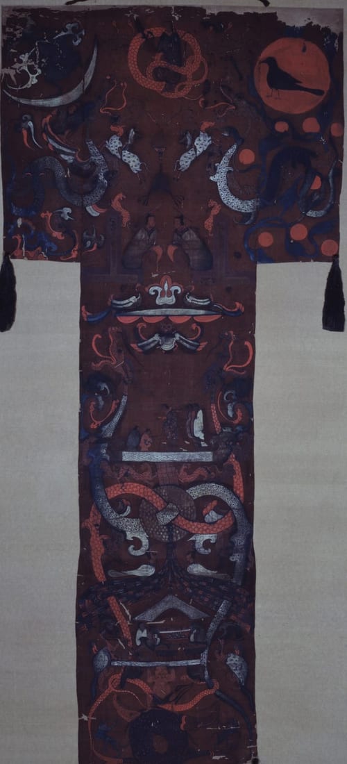 一幅深红褐色丝绢上的 T 形画：上部横宽，右上角是一轮红日，日中站着一只黑鸟；左上角是一弯白色新月；中间有一个红色盘曲的人首蛇身像。下面竖长的部分里，有一个拄杖的妇人和侍从，一块被两条龙穿过的璧，再往下是摆着器物的场景，最底下一个人托起一块平台。